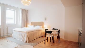 A modern bedroom with a large bed, bedside table, and a small dining area with chairs.