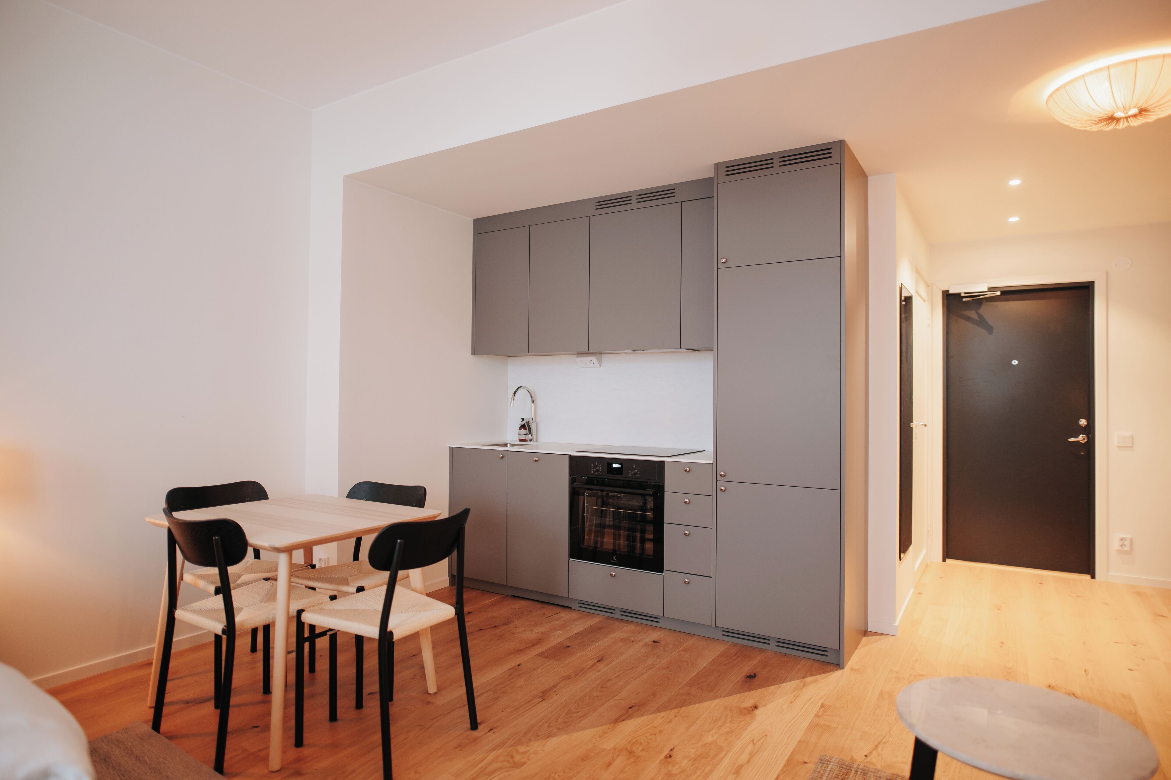 A compact kitchen with grey cabinets, a built-in oven, and a dining area with a table and chairs.