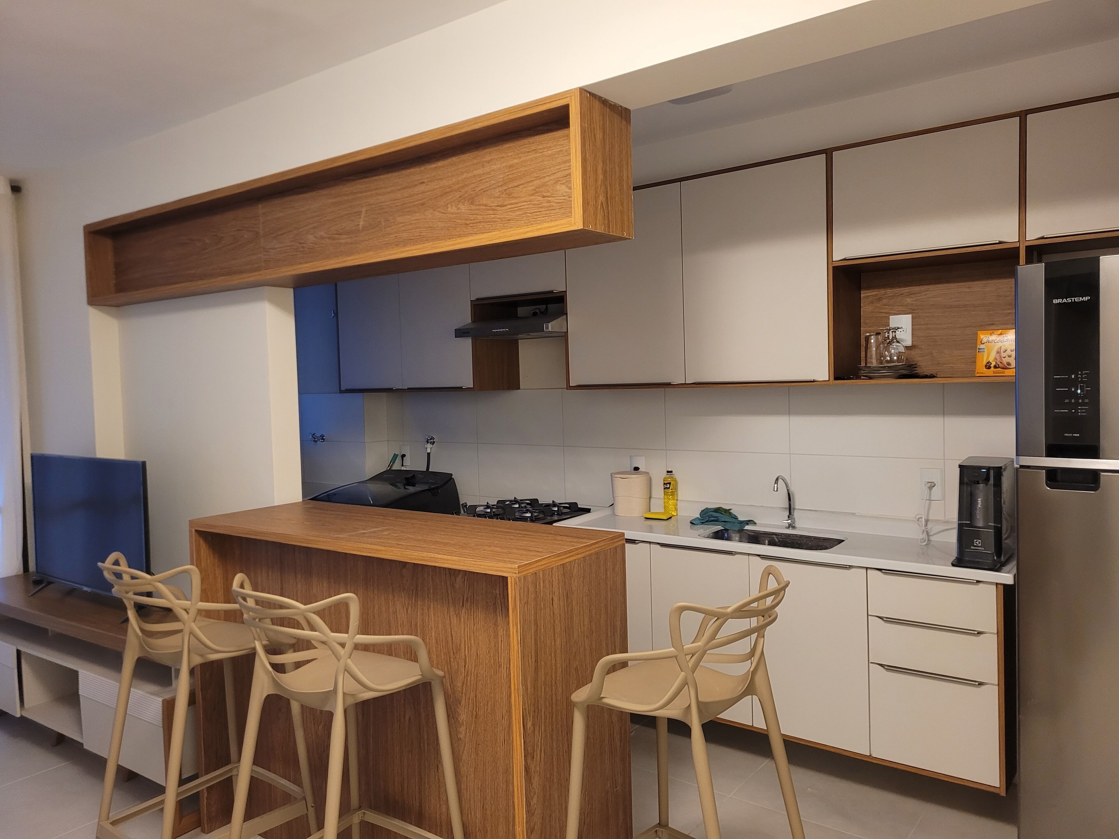 Une cuisine moderne avec un îlot central en bois, des tabourets de bar, un réfrigérateur en acier inoxydable et des meubles de cuisine blancs.
