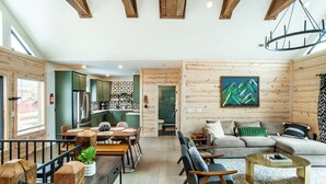 Un vaste espace de vie comprenant un canapé, des fauteuils et une table basse. On y trouve également un coin repas avec une table et des chaises. Les murs de la pièce sont en bois et le plafond est orné de poutres apparentes.