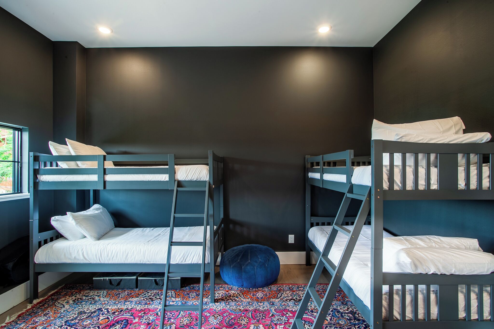 A bunk bed room with a patterned rug, dark walls, and a window.