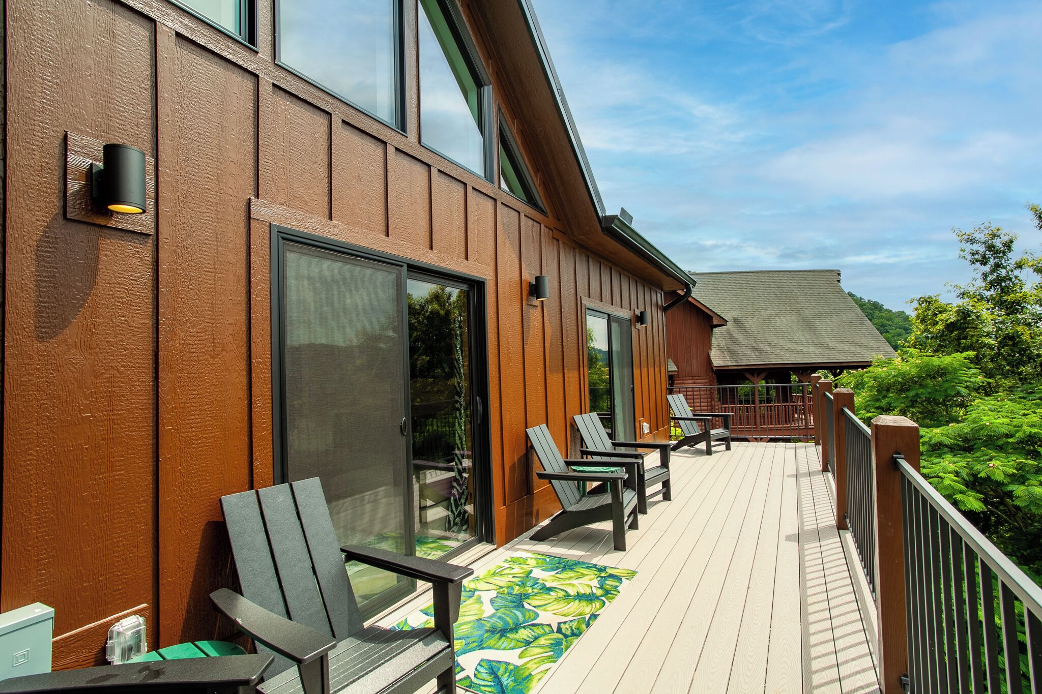 Una terraza de madera con mobiliario exterior y una puerta de vidrio que da a un espacio cubierto.