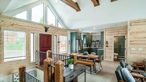 Une cuisine spacieuse avec des poutres en bois, un coin repas avec un banc et un salon doté d’un canapé.