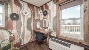 A room with a patterned wallpaper, a desk with a chair, a large window with a view, and a radiator. - Extended Stay | Spacious Kitchen Studio | Free Parking (Prescott)