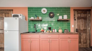 A kitchen with a white refrigerator, a sink, and a countertop with various items. There are two wooden cabinets and a green tiled backsplash. - Extended Stay | Spacious Kitchen Studio | Free Parking (Prescott)