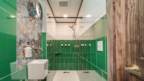 A modern bathroom with green tiles, a white sink, and a shower with a glass door. - Extended Stay | Spacious Kitchen Studio | Free Parking (Prescott)