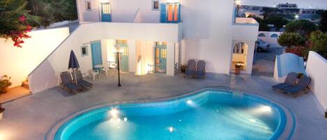 A modern building with a swimming pool, lounge chairs, and a view of the surrounding area.