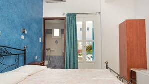 A bedroom with a bed, a wooden wardrobe, a bathroom with a shower, and a view of the outside.