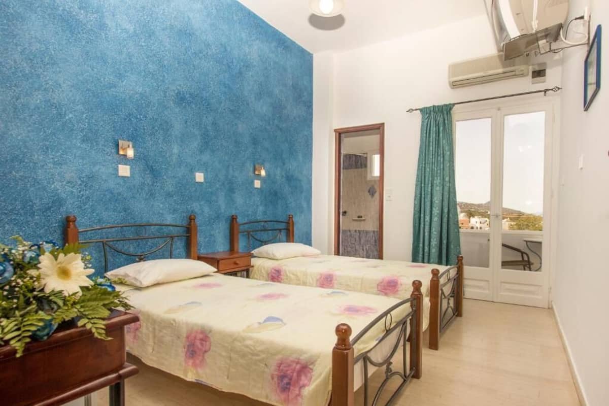 Een slaapkamer met twee bedden, een houten hoofdeinde, een nachtkastje, een potplant en een balkon met uitzicht.