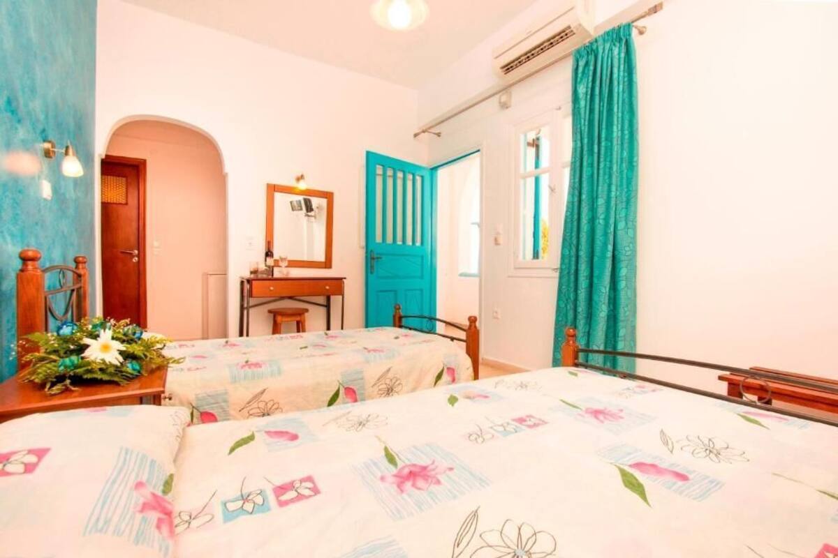 Een kamer met twee bedden, een houten bureau, een spiegel en een raam met turquoise gordijnen.