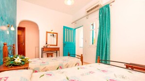 A room with two beds, a wooden desk, a mirror, and a window with teal curtains. - Villa Pelekanos Santo (Santorini)