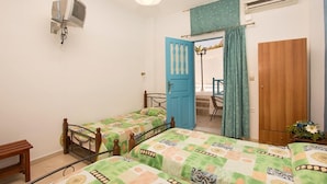 A bedroom with two single beds, a wooden wardrobe, a small table, a TV mounted on the wall, and a door leading to a balcony. - Villa Pelekanos Santo (Santorini)