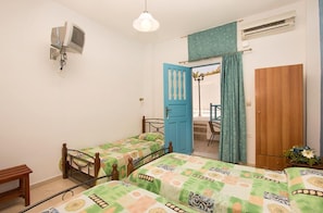 A bedroom with two single beds, a wooden wardrobe, a small table, a TV mounted on the wall, and a door leading to a balcony. - Villa Pelekanos Santo (Santorini)