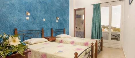A bedroom with two beds, a wooden headboard, a nightstand, a potted plant, and a balcony with a view.