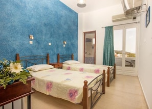 A bedroom with two beds, a wooden headboard, a nightstand, a potted plant, and a balcony with a view. - Villa Pelekanos Santo (Santorini)