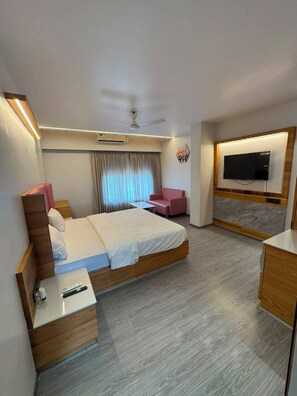Una habitación de hotel moderna con cama, mesita de noche, televisión y un área de descanso.