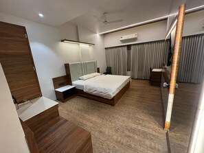 A modern bedroom with a wooden bed frame, a bedside table, a nightstand, a large mirror, an air conditioning unit, and a ceiling fan. - Hotel Geetanjali (Pipariya)