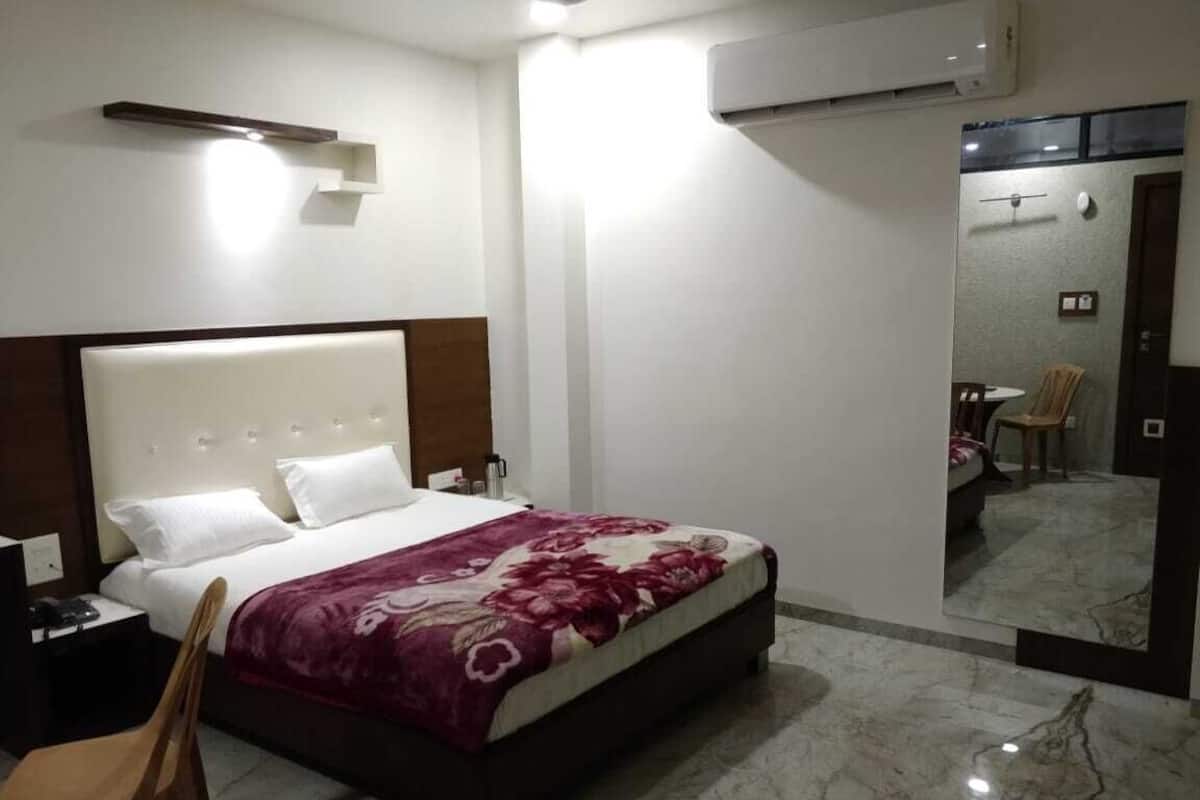 A hotel room with a bed, a chair, a nightstand, an air conditioning unit, and a mirror.