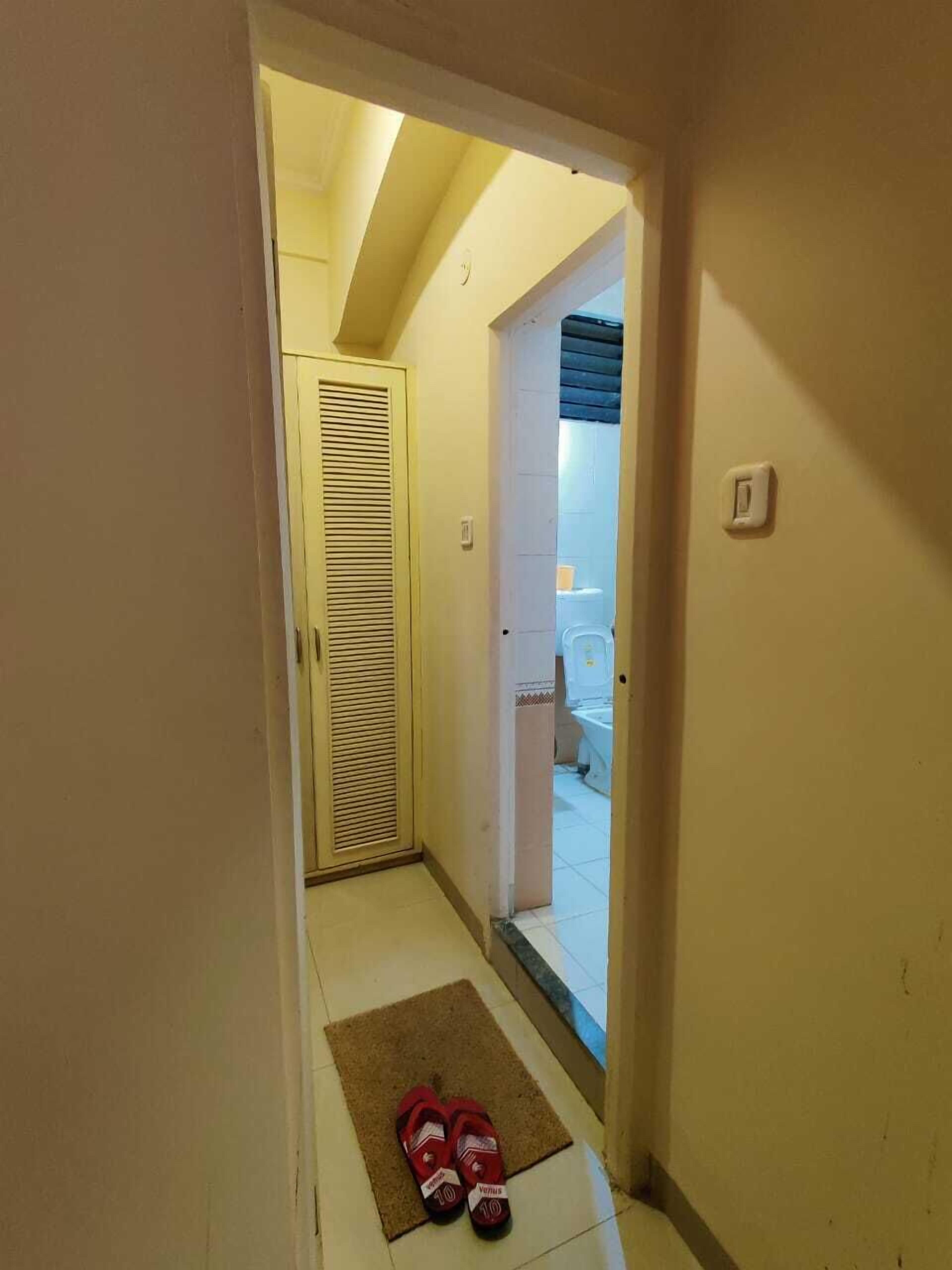Een gang met een deur naar een badkamer, een deurmat en slippers op de vloer.