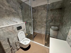 A modern bathroom with a glass-enclosed shower, a white toilet, and a marble wall. - Hotel Geetanjali (Pipariya)