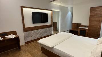 A modern hotel room with a large bed, a flat-screen TV mounted on the wall, a wooden nightstand, and a desk with a lamp.