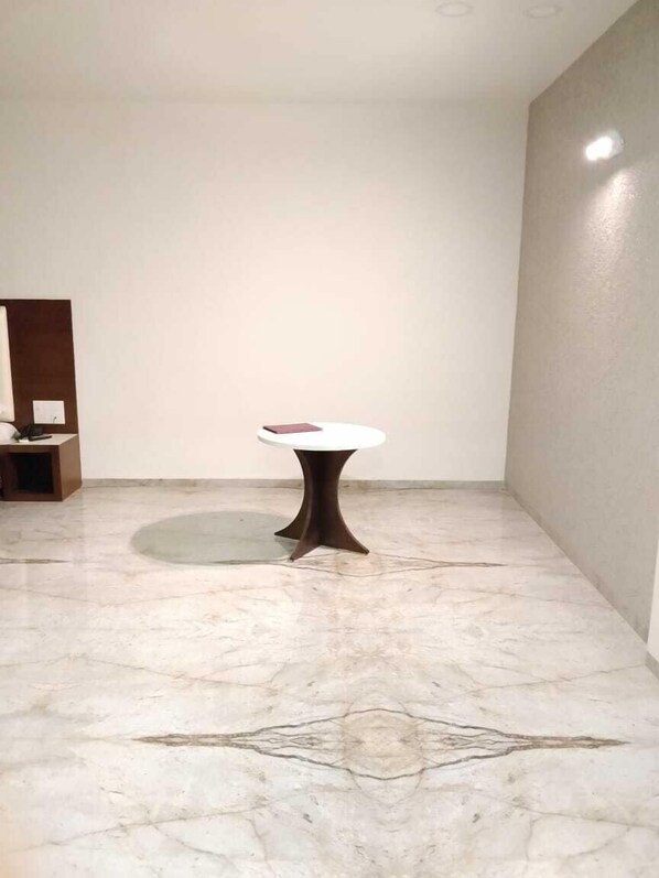 A room with a marble floor, a round table with a dark base, and a white wall. - Hotel Geetanjali (Pipariya)