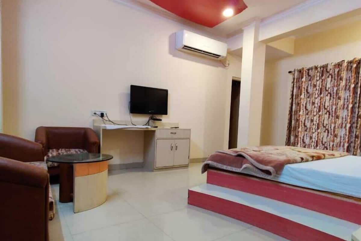 A bedroom with a bed, a desk, a chair, a television, and an air conditioning unit.