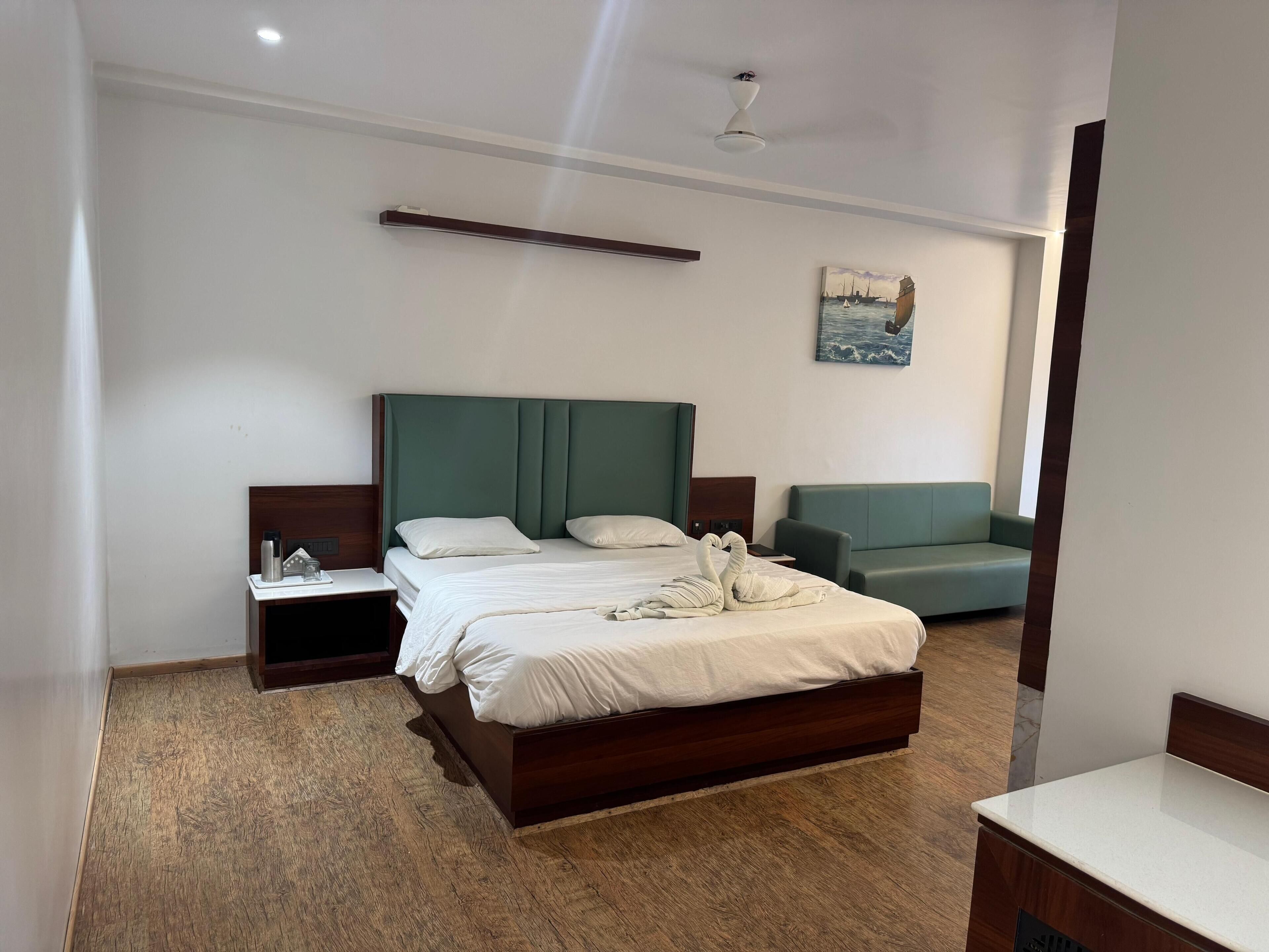 Habitación de hotel con una cama grande, una mesita de noche, un sofá verde y un cuadro en la pared.