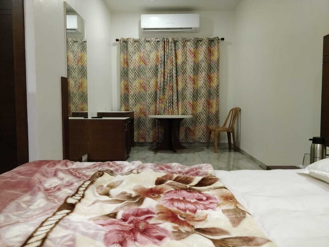 Quarto de hotel com cama, escrivaninha, cadeira, espelho e área de chuveiro.
