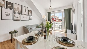A modern living room with a dining area, featuring a white table set for four, a sofa, and a cityscape wall art. - Vacation apartment Hirschegg, 2 x bath 5Z 10 beds kitchen 2 parking spaces, WLAN (Bad Friedrichshall)