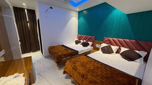 A hotel room with two beds, a ceiling fan, a wooden table, and a view of the outside. - Hotel Madhuban (Khuldabad)