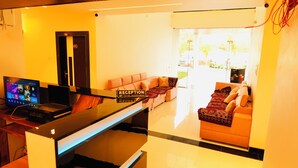 A reception area with a reception desk, a laptop, a flat-screen TV, and a sofa with a patterned throw. - Hotel Madhuban (Khuldabad)