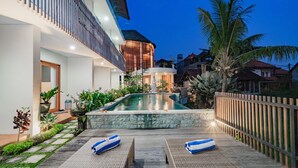 A modern outdoor pool area with a statue, surrounded by lush greenery and a wooden fence. - Juli House (Ubud)