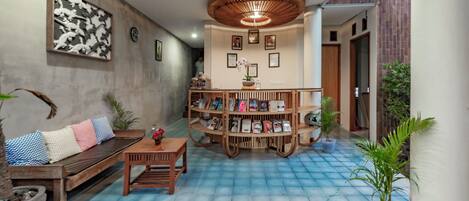 A modern living room with a blue-tiled floor, a wooden bookshelf, a sofa with patterned cushions, and a ceiling light fixture.