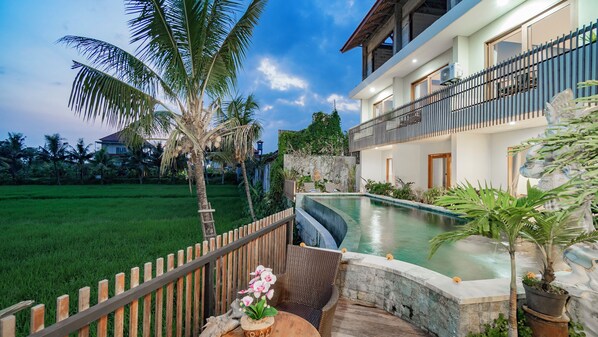 Ein zweistöckiges Haus mit Swimmingpool, Holzzaun und Garten mit Palmen.