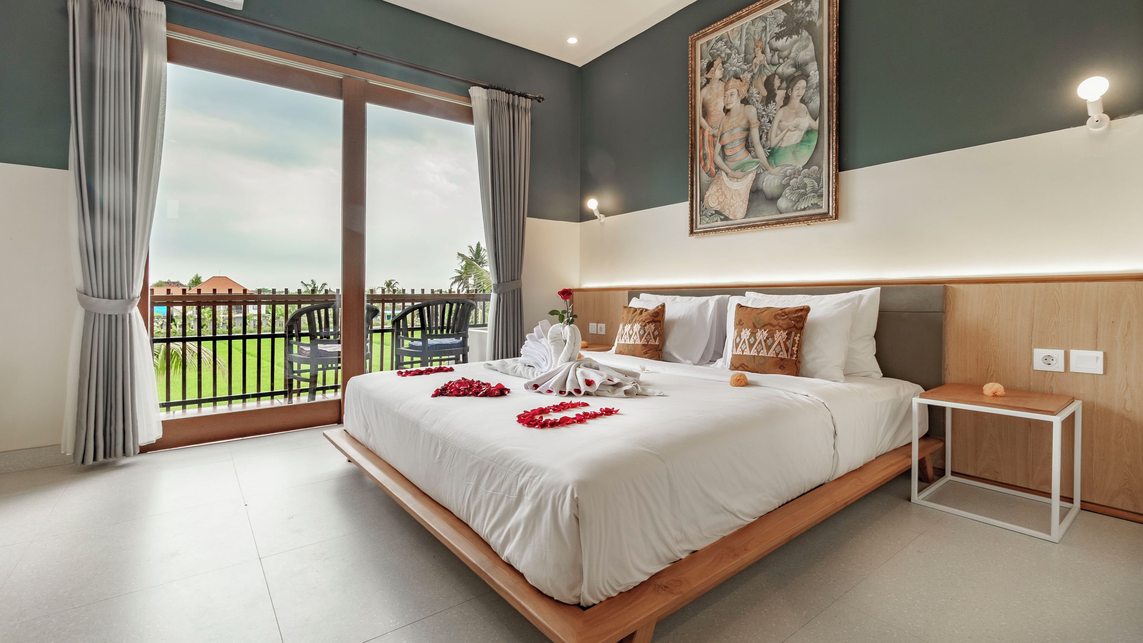 Een hotelkamer met een groot bed, een klein nachtkastje, een schilderij aan de muur en een balkon met uitzicht op de lucht en groen.
