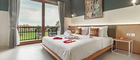 Een hotelkamer met een groot bed, een klein nachtkastje, een schilderij aan de muur en een balkon met uitzicht op de lucht en groen.
