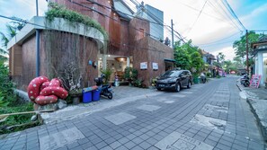 A street view with a building labeled "Jill House" on the left, a parked car, and a motorcycle. - Juli House (Ubud)
