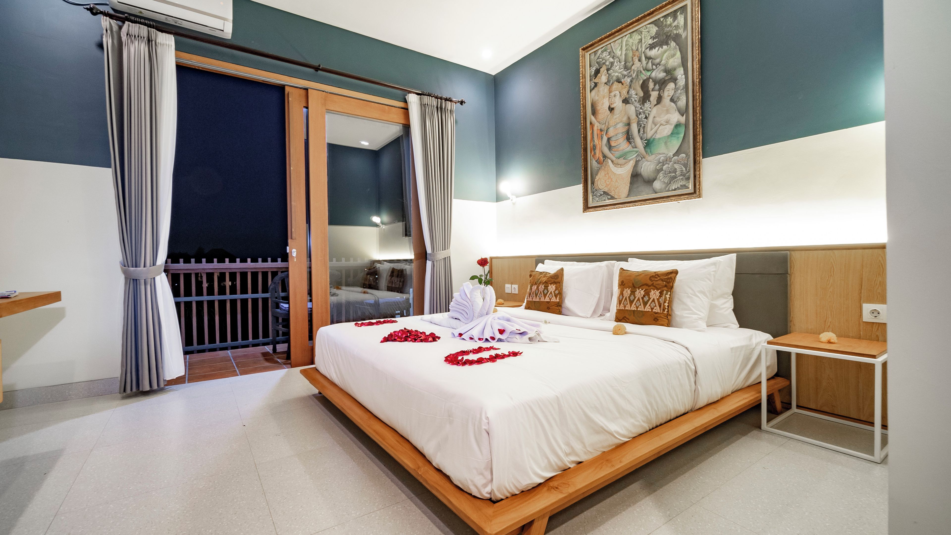 Quarto de hotel com cama, mesa de cabeceira, quadro e varanda com cortinas.