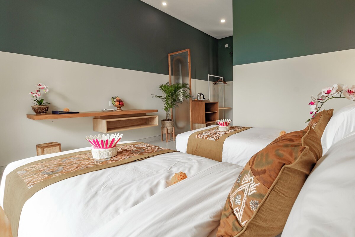 A hotel room with two beds, a wooden shelf with a potted plant, a mirror, and a hanging plant.