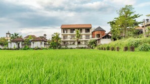 A residential area with houses, a large green field, and a cloudy sky. - Juli House (Ubud)