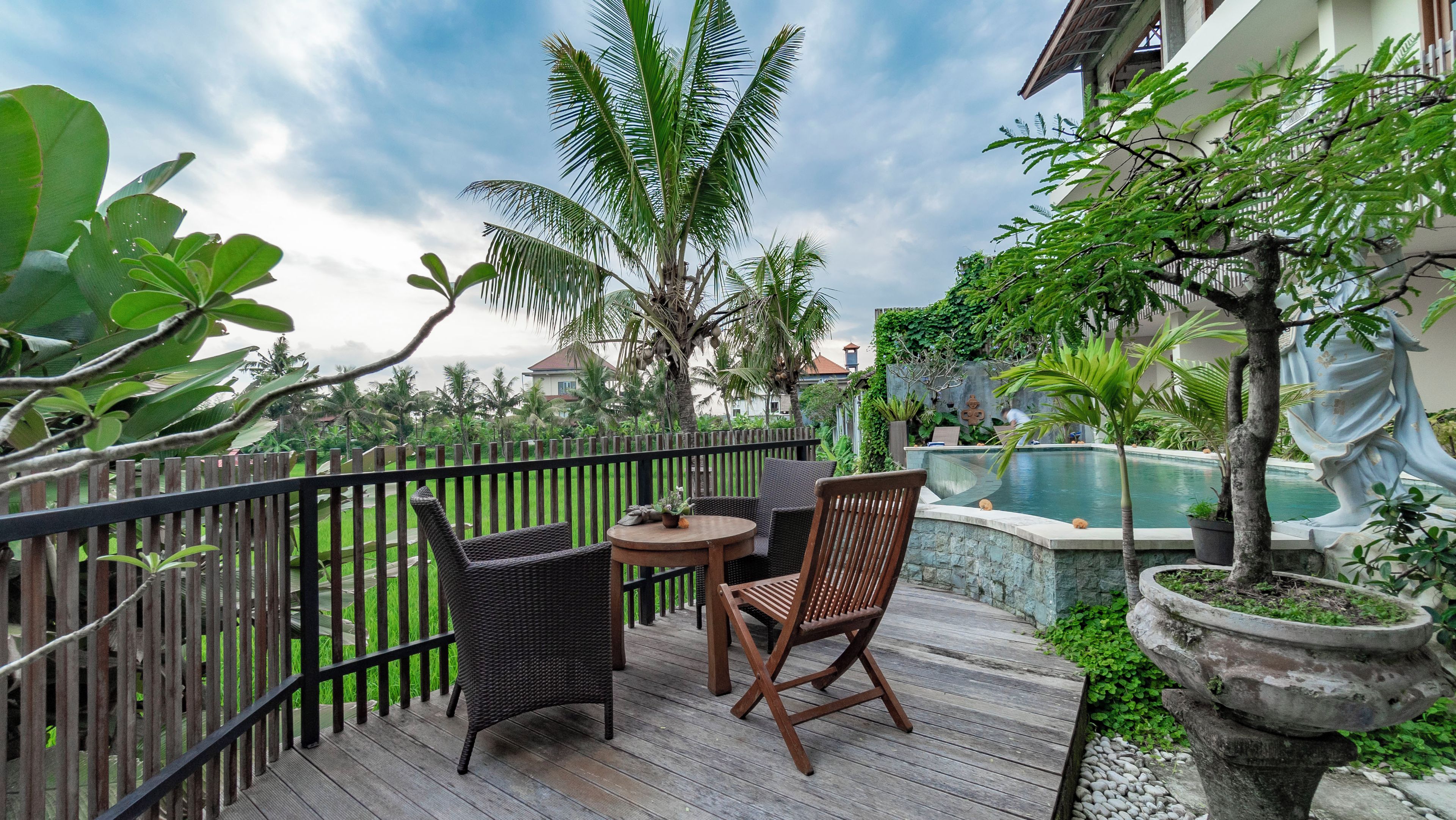 A wooden deck with wicker furniture, a pool, and tropical plants.