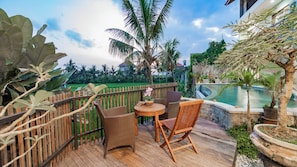 A wooden deck with wicker furniture, a small round table, and a potted plant. - Juli House (Ubud)