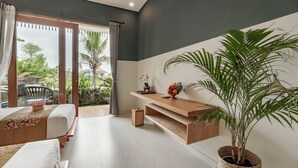 A modern hotel room with a balcony, a bed, a desk, and a large potted plant. - Juli House (Ubud)