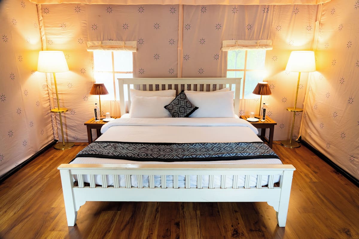 A neatly made bed with a patterned throw, two bedside lamps, and a nightstand with a bottle.