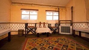 Une pièce avec un sol à motifs, deux fenêtres avec des rideaux, une table recouverte d’une nappe et un lit avec une couvre-lit à motifs.