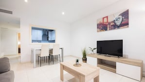 Una sala de estar moderna con televisor, un comedor y una cocina al fondo.