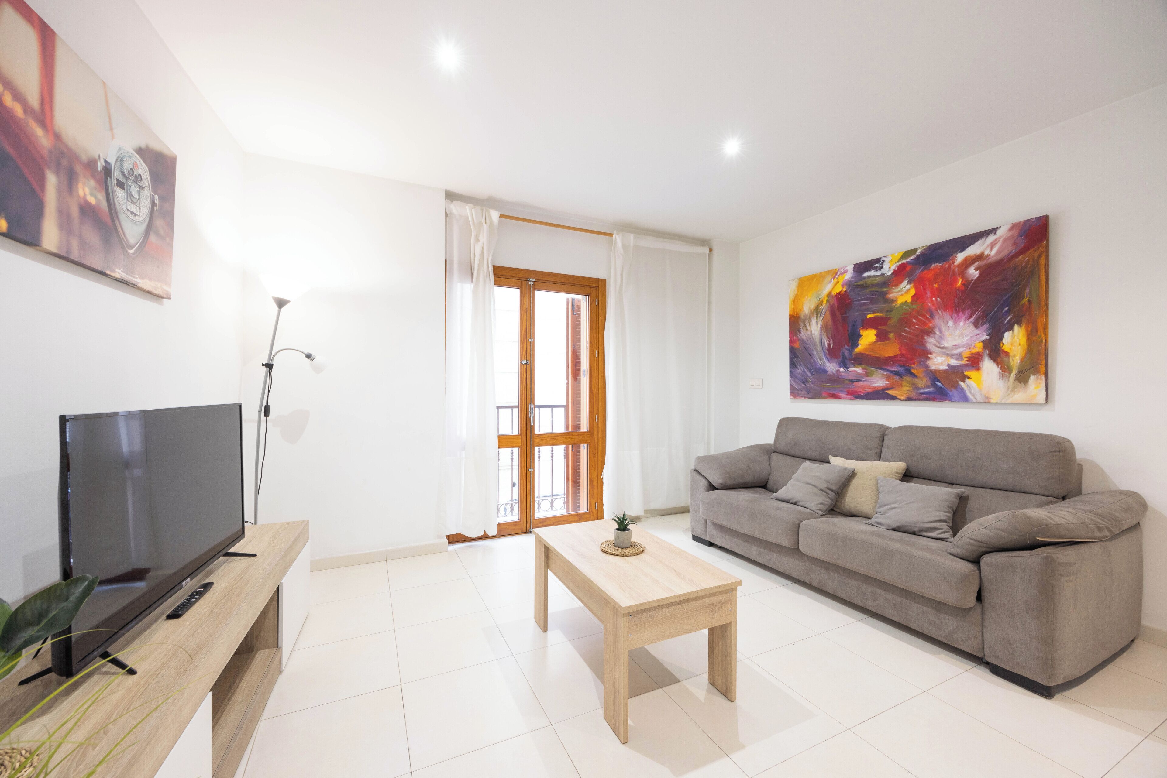 Una sala de estar moderna con un televisor de pantalla plana, una mesa de centro de madera, un sofá gris y un cuadro abstracto colorido.