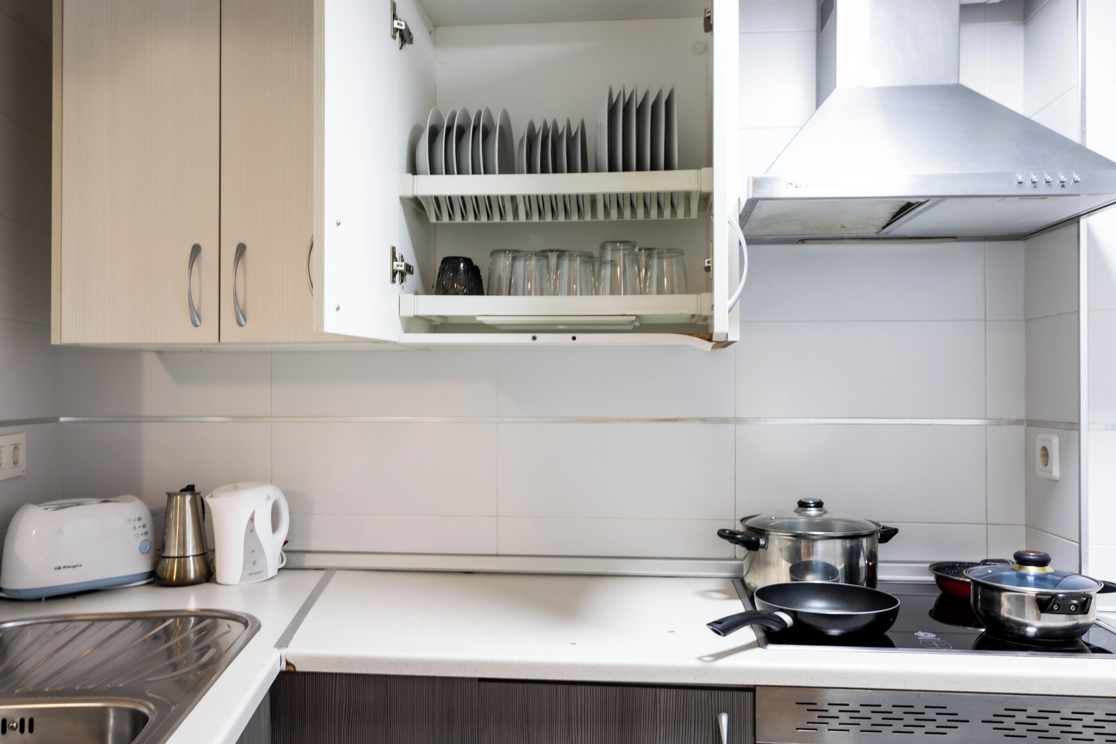 A kitchen with white cabinets, a toaster, a kettle, a coffee maker, and a stove with pots and pans.