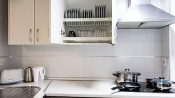 A kitchen with white cabinets, a toaster, a kettle, a coffee maker, and a stove with pots and pans.